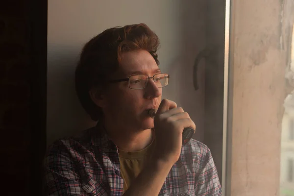Hombre joven fumando cigarrillo electrónico cerca de la ventana . — Foto de Stock