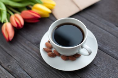 Beyaz fincan kahve siyah ahşap zemin üzerine sarı ve turuncu Lale ile