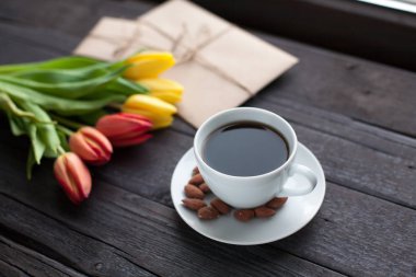 Beyaz fincan kahve siyah ahşap zemin üzerine sarı ve turuncu Lale ile