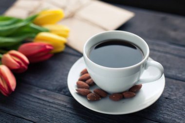 Beyaz fincan kahve siyah ahşap zemin üzerine sarı ve turuncu Lale ile