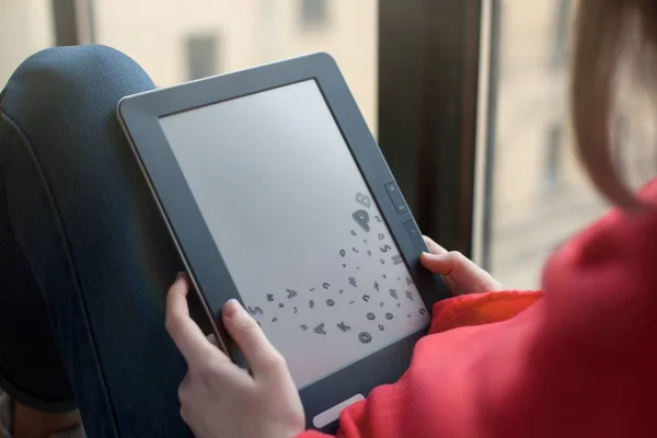 A woman sits by the window and uses an e-book. blank screen — Stock Photo, Image