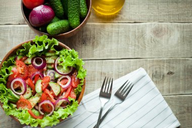 Salata taze domates, salatalık, kırmızı soğan ve marul, ahşap bir kapta zeytinyağı ve karabiber ile giyinmiş. Üstten Görünüm