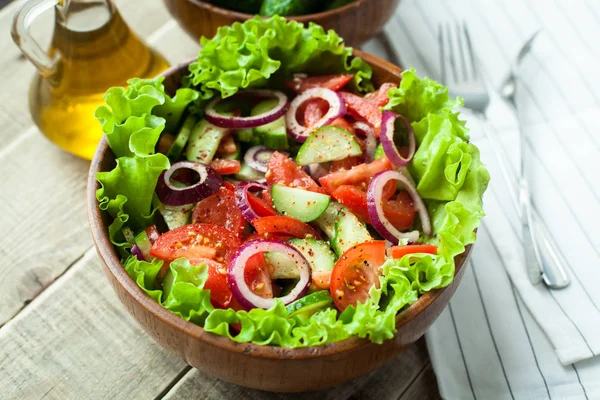 Rustieke salade van verse tomaten, komkommer, rode uien en sla, gekleed met olijfolie en peper in een houten kom. Bovenaanzicht — Stockfoto