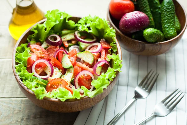 Rustieke salade van verse tomaten, komkommer, rode uien en sla, gekleed met olijfolie en peper in een houten kom. Bovenaanzicht — Stockfoto