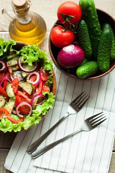 Rustieke salade van verse tomaten, komkommer, rode uien en sla, gekleed met olijfolie en peper in een houten kom. Bovenaanzicht — Stockfoto