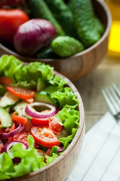 Rustieke salade van verse tomaten, komkommer, rode uien en sla, gekleed met olijfolie en peper in een houten kom. Bovenaanzicht — Stockfoto