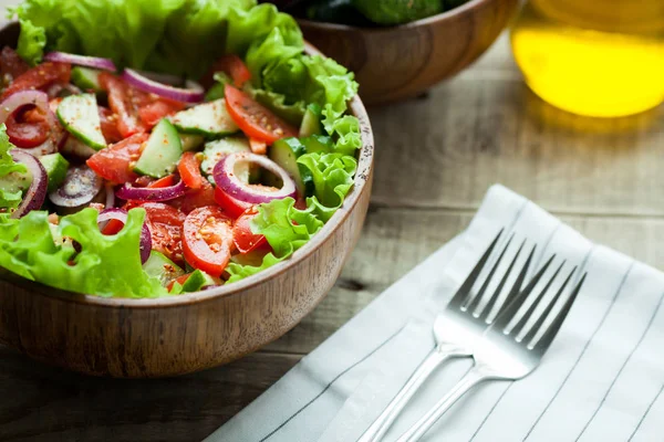 Rustieke salade van verse tomaten, komkommer, rode uien en sla, gekleed met olijfolie en peper in een houten kom. Bovenaanzicht — Stockfoto