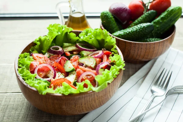 Rustic salad of fresh tomatoes, cucumbers, red onions and lettuce, dressed with olive oil and ground pepper in a wooden bowl. Top view — Stock Photo, Image