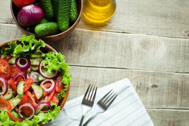Salata taze domates, salatalık, kırmızı soğan ve marul, ahşap bir kapta zeytinyağı ve karabiber ile giyinmiş. Üstten Görünüm