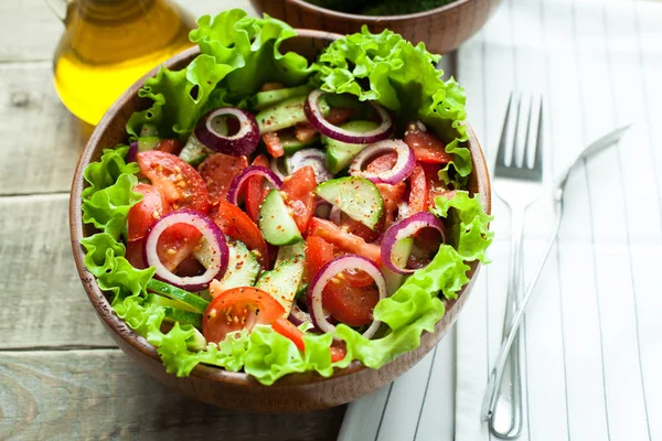 Salada rústica de tomates frescos, pepinos, cebolas vermelhas e alface, vestida com azeite e pimenta moída em uma tigela de madeira. Vista superior — Fotografia de Stock