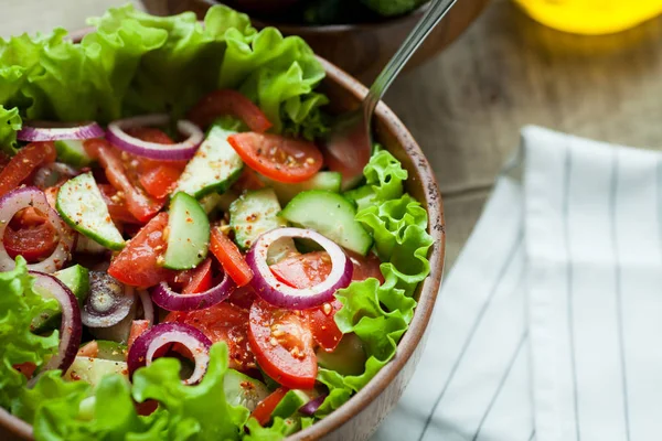 Rustieke salade van verse tomaten, komkommer, rode uien en sla, gekleed met olijfolie en peper in een houten kom. Bovenaanzicht — Stockfoto