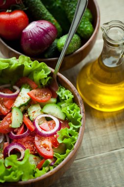 Rustik salata taze domates, salatalık, kırmızı soğan ve marul, ahşap bir kapta zeytinyağı ve karabiber ile giyinmiş. Üstten Görünüm