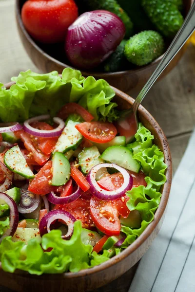 Rustieke salade van verse tomaten, komkommer, rode uien en sla, gekleed met olijfolie en peper in een houten kom. Bovenaanzicht — Stockfoto