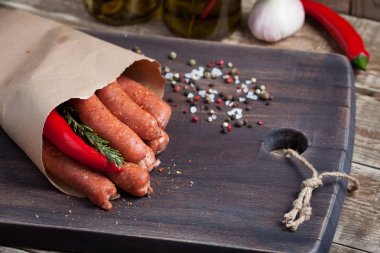 Biberiye ve bir siyah ahşap tahta üzerinde bir kağıt zarf içinde chili biber soslu kuzu ham ev yapımı sosis