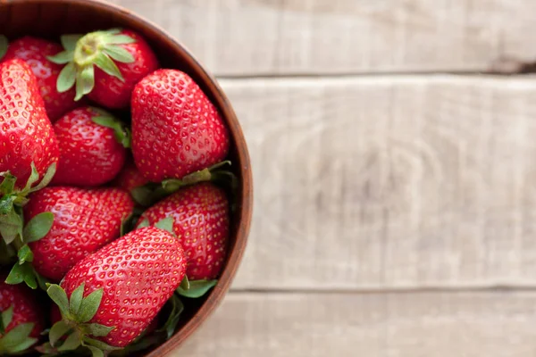 Ahşap bir masa üzerinde bir ahşap kase taze çilek.