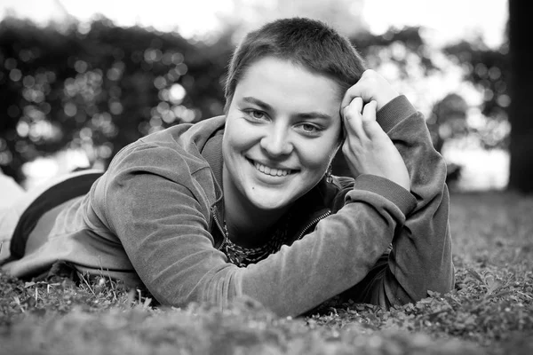 Retrato de uma menina bonita com cabelo curto e olhos verdes jaz na grama, sorrindo e olhando para a câmera — Fotografia de Stock