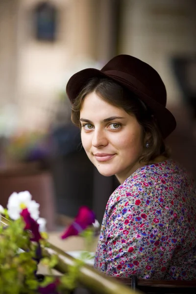 Όμορφη νεαρή γυναίκα σε ένα καπέλο με ένα φλυτζάνι του τσαγιού που κάθεται σε μια καφετέρια, κοιτάζοντας την κάμερα και να χαμογελά — Φωτογραφία Αρχείου