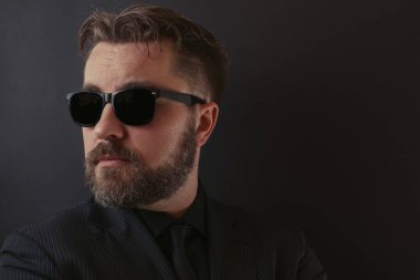 Sakal ve şık bir saç modeli siyah bir takım elbise ve güneş gözlüğü ile acımasız bir adam