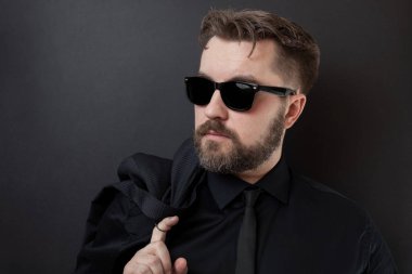 Sakal ve siyah gömlek ve kravat şık bir saç modeli ile acımasız bir adam onun ceketi tutuyor. Siyah bir arka plan iş başında zor bir günün ardından genç iş adamı