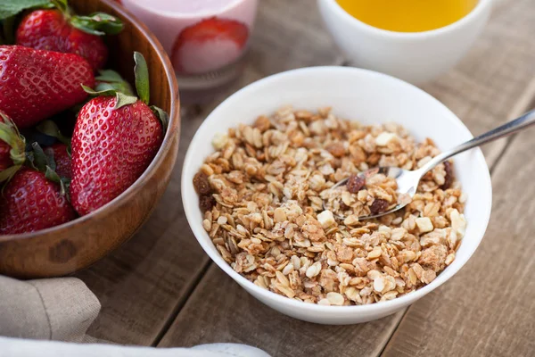 A bowl of homemade granola with yogurt and fresh strawberries on a wooden background. Healthy breakfast with green tea — Stock Photo, Image