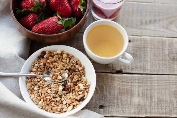 Чаша домашней мюсли с йогуртом и свежей клубникой на деревянном фоне. Здоровый завтрак с зеленым чаем — стоковое фото