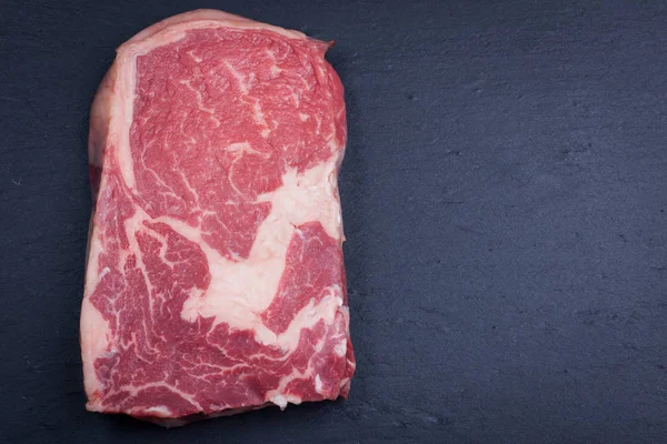 Mármore cru, carne fresca, bife Angus ribeye preto sobre um fundo de pedra escura . — Fotografia de Stock