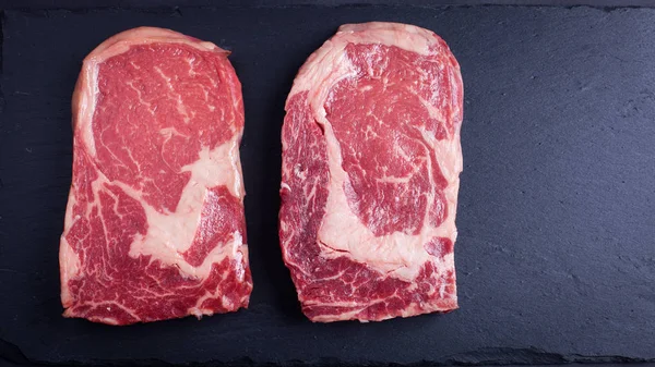 Dos carnes frescas de mármol crudo, filete negro Angus ribeye sobre un fondo de piedra oscura . —  Fotos de Stock