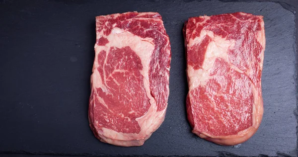 Dvě čerstvé syrové mramorové maso, black Angus ribeye steak na tmavém pozadí kamene. — Stock fotografie