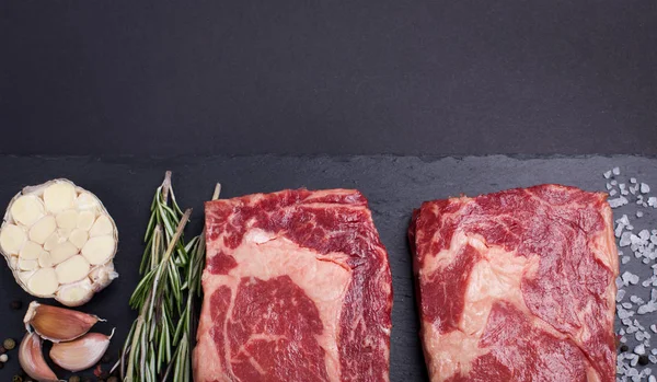 Dvě čerstvé syrové mramorové maso, black Angus ribeye steak s kořením na tmavém pozadí kamene. — Stock fotografie