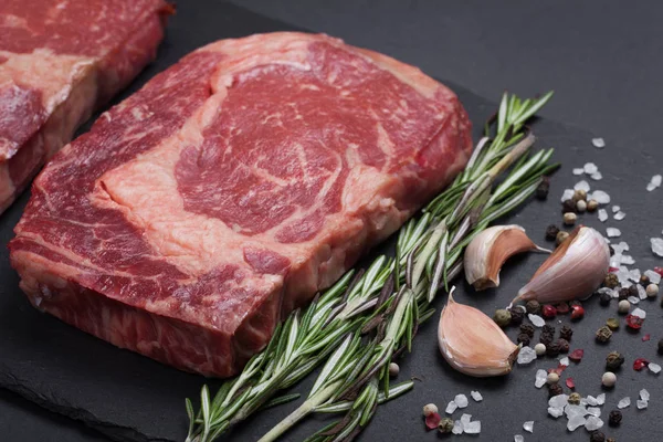 一块新鲜原料的黑安格斯大理石纹肉与香料特写石头黑色背景。肋眼牛排 — 图库照片