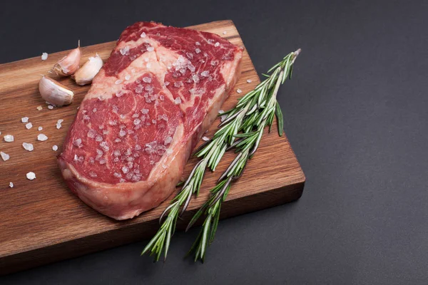 Kousek čerstvého syrového black angus mramorované maso s kořením close-up na kámen tmavém pozadí. Ribeye steak — Stock fotografie