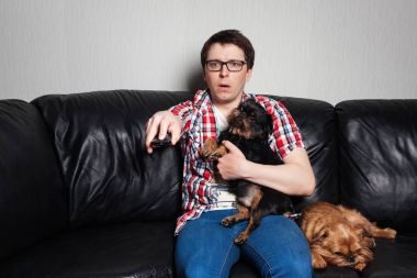 Portre portre, kırmızı gömlekli, iki köpek, tarassut Tv, uzaktan kumanda, holding ile siyah deri kanepede oturan genç adam ne görürse şaşırttı. O sürpriz bir siyah köpek yakaladı