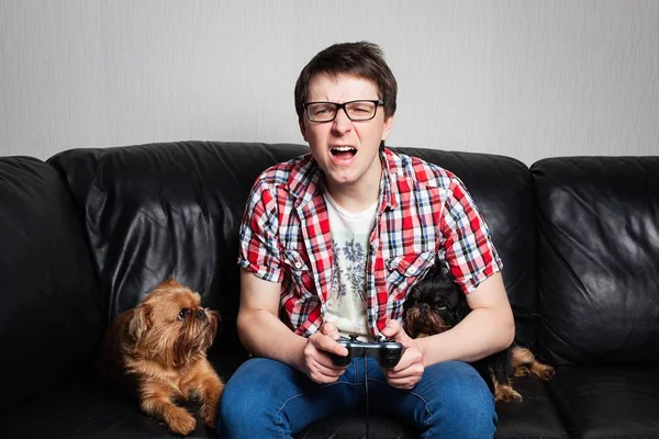 Um jovem de camisa vermelha e jeans azul senta-se em casa e joga videogames junto com seu cachorro. Garoto gritando na frente da TV tentando lutar com seus inimigos. Cão olhando para seu mestre — Fotografia de Stock