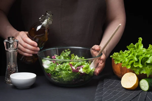 Mujer chef en la cocina preparando ensalada de verduras. Alimentación Saludable. Concepto de dieta. Una forma de vida saludable. Para cocinar en casa. La chica va a regar la lechuga con aceite de oliva sobre un fondo oscuro — Foto de Stock