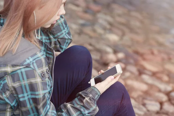 Jovem menina bonita sentada na praia e ouvir música em seu smartphone — Fotografia de Stock