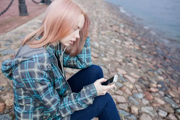 Fiatal gyönyörű lány ül a strandon, és hallgató-hoz zene-ra-a smartphone — Stock Fotó
