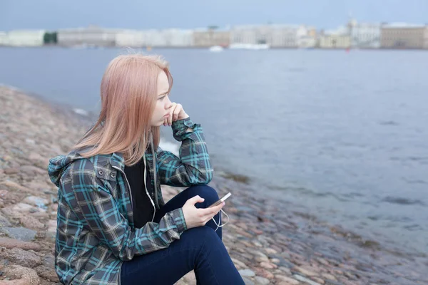 Junges schönes Mädchen, das am Strand sitzt und Musik auf dem Smartphone hört. sie ruht und denkt — Stockfoto