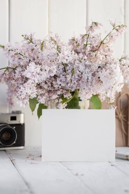 Lila çiçek buketi ve zarf ile beyaz ahşap zemin üzerinde vintage fotoğraf makinesi ile boş beyaz tebrik kartı. yukarı alay
