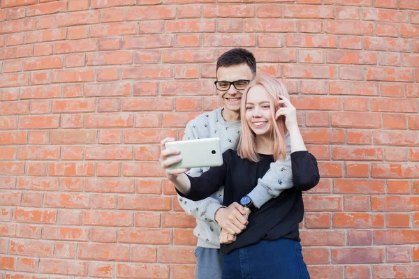 年轻夫妇拍摄与背景的红砖墙上智能手机的拍照 — 图库照片