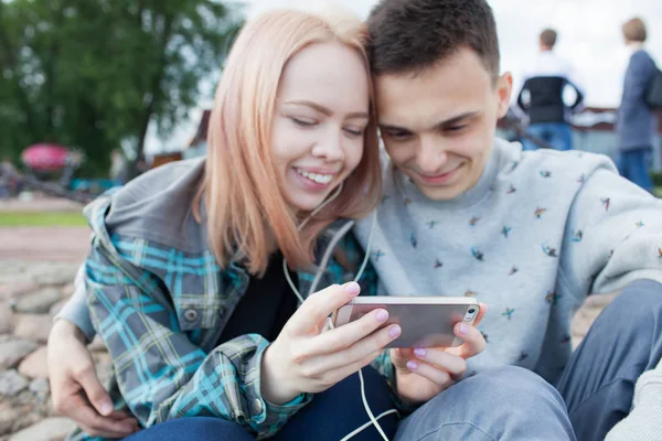 年轻夫妇观看视频，在河边的沙滩上的智能手机。他们的微笑，看到有趣的视频 — 图库照片