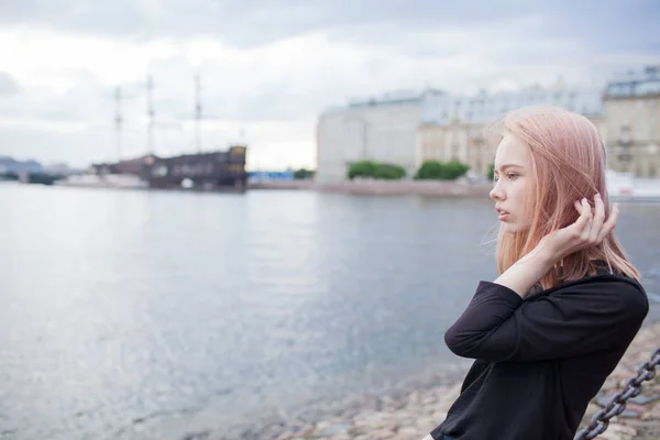 Menina bonita jovem sentado na costa e endireita o cabelo. No fundo está desfocado velho navio — Fotografia de Stock