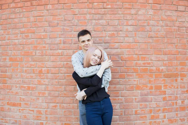 Happy young couple hugging and smiling on a background of red brick wall. Blonde girl with blue eyes and a young man of Arab appearance with brown eyes — Stock Photo, Image