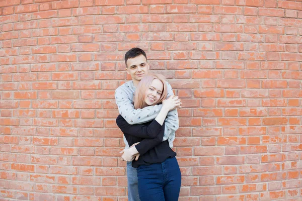 Feliz casal jovem abraçando e sorrindo em um fundo de parede de tijolo vermelho. Menina loira com olhos azuis e um jovem de aparência árabe com olhos castanhos — Fotografia de Stock