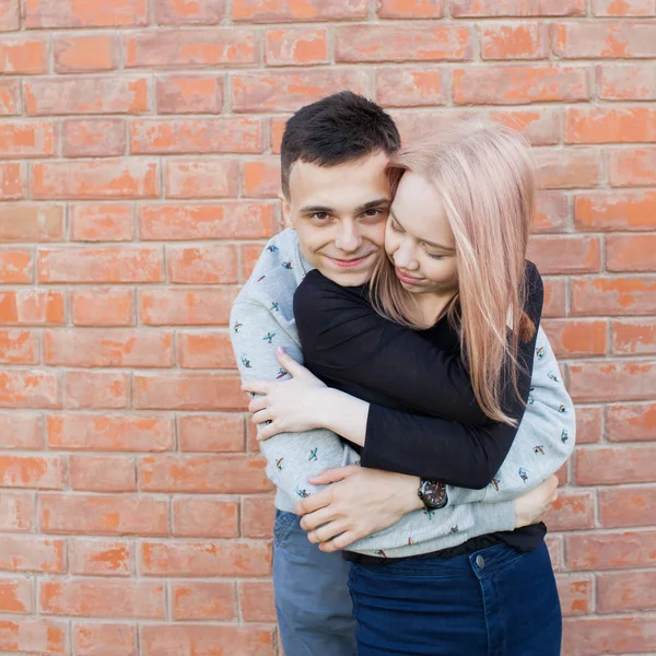 Feliz casal jovem abraçando e sorrindo em um fundo de parede de tijolo vermelho. Menina loira com olhos azuis e um jovem de aparência árabe com olhos castanhos — Fotografia de Stock