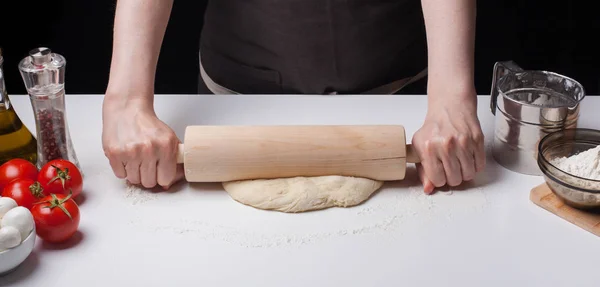 Masa de pizza enrollada a mano femenina con un rodillo sobre una mesa blanca, espolvoreada con harina — Foto de Stock