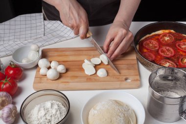 Bir kadın Şef bir İtalyan ev yapımı pizza yapmak için mozzarella peyniri dilimleri. Mozzarella peyniri, pizza hamuru ve sarımsak beyaz masaya vardır