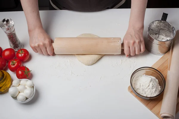 Masa de pizza enrollada a mano femenina con un rodillo sobre una mesa blanca, espolvoreada con harina — Foto de Stock