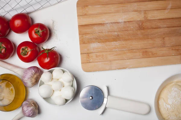 Tabla de cortar de madera con ingredientes para pizza casera en una mesa blanca — Foto de Stock