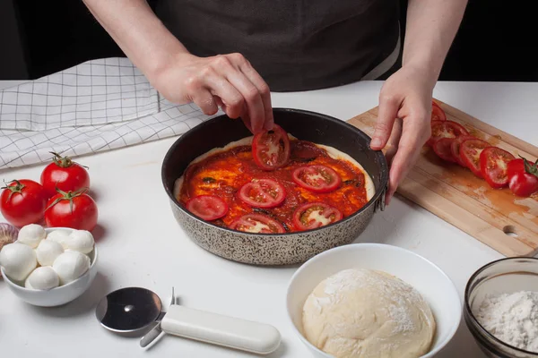La chef añade tomates para hacer pizza casera. En la mesa blanca hay mozzarella, masa de pizza — Foto de Stock