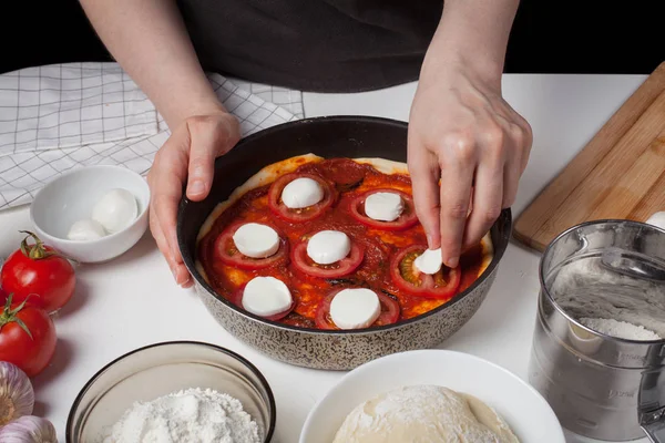 La chef añade queso a la mozzarella para hacer pizza casera. En la mesa blanca hay mozzarella, masa de pizza y ajo. . — Foto de Stock